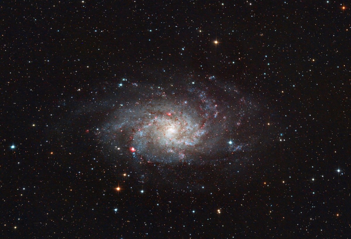 Die Dreiecksgalaxie Messier 33 mit ihren Spiralarmen und roten Nebelgebieten.